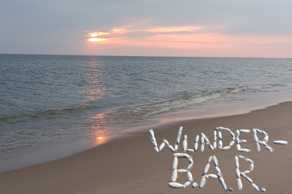 Strandszene mit Sonnenuntergang. Schriftzug Wunder-B.A.R. mit Schulpen ausgelegt