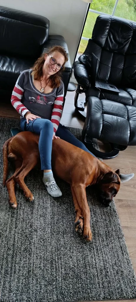 Rhodesian Ridgeback Floyd liegt entspannt quer unter einem Bein von Katja, die im Ferienhaus in Dänemark auf dem Teppich sitzt